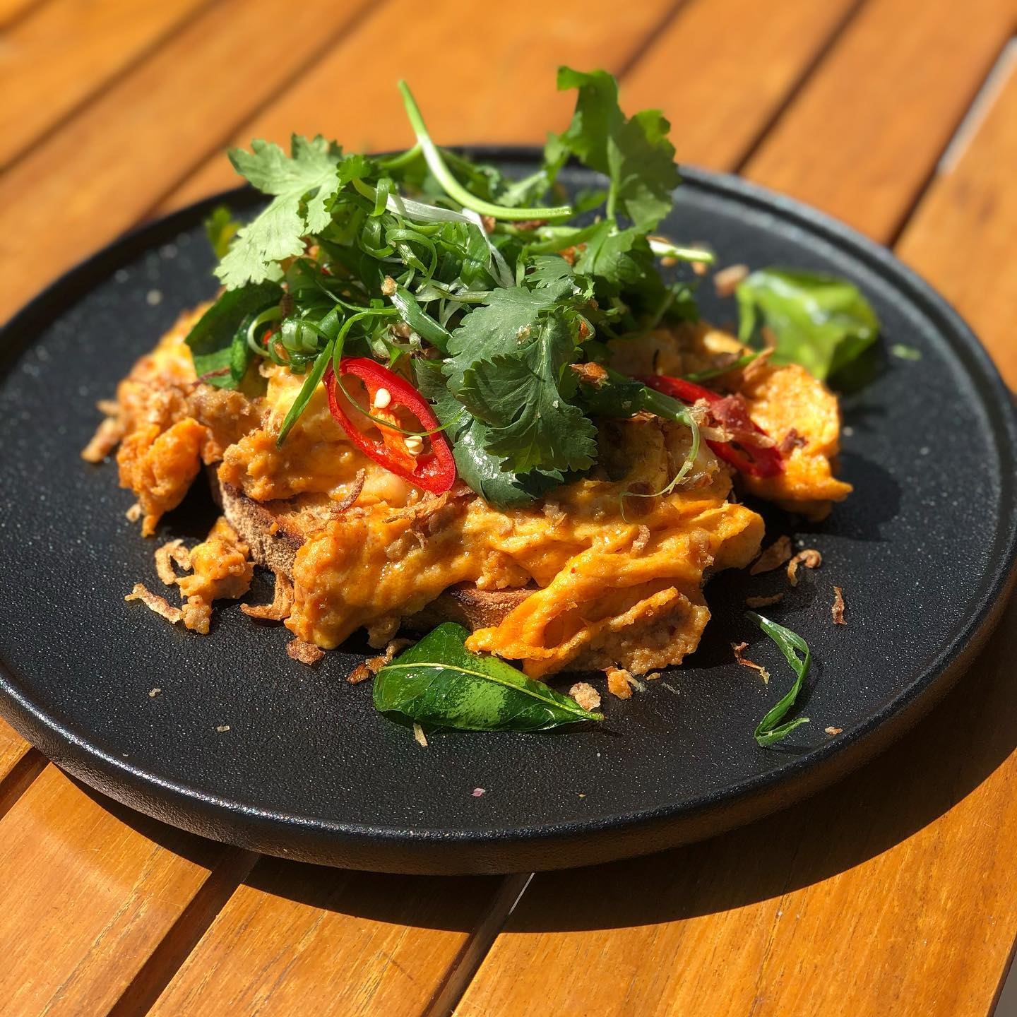 Crispy chicken with fresh herbs and chilli on a dark plate outside