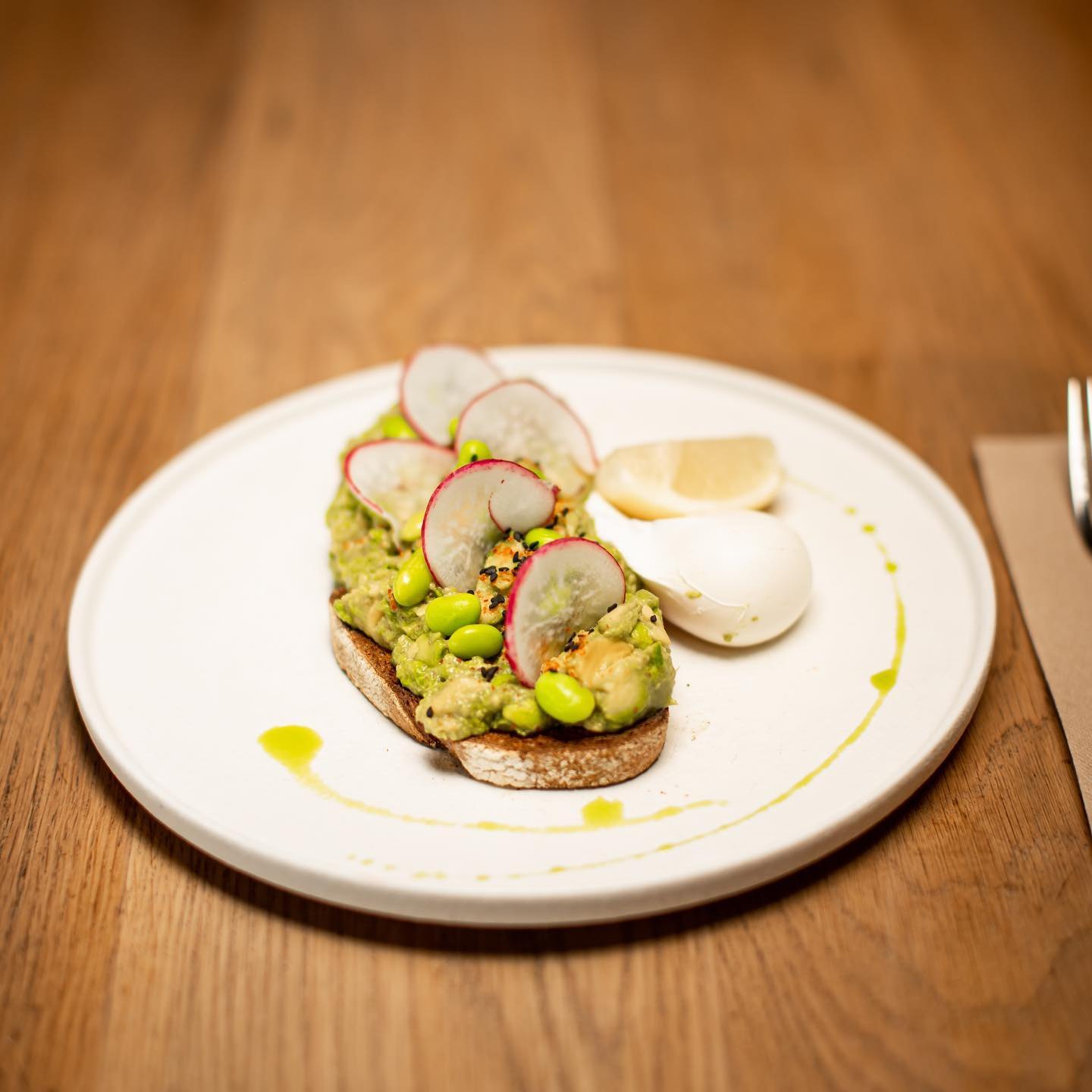 Avocado toast with radish and a poached egg on a timber table