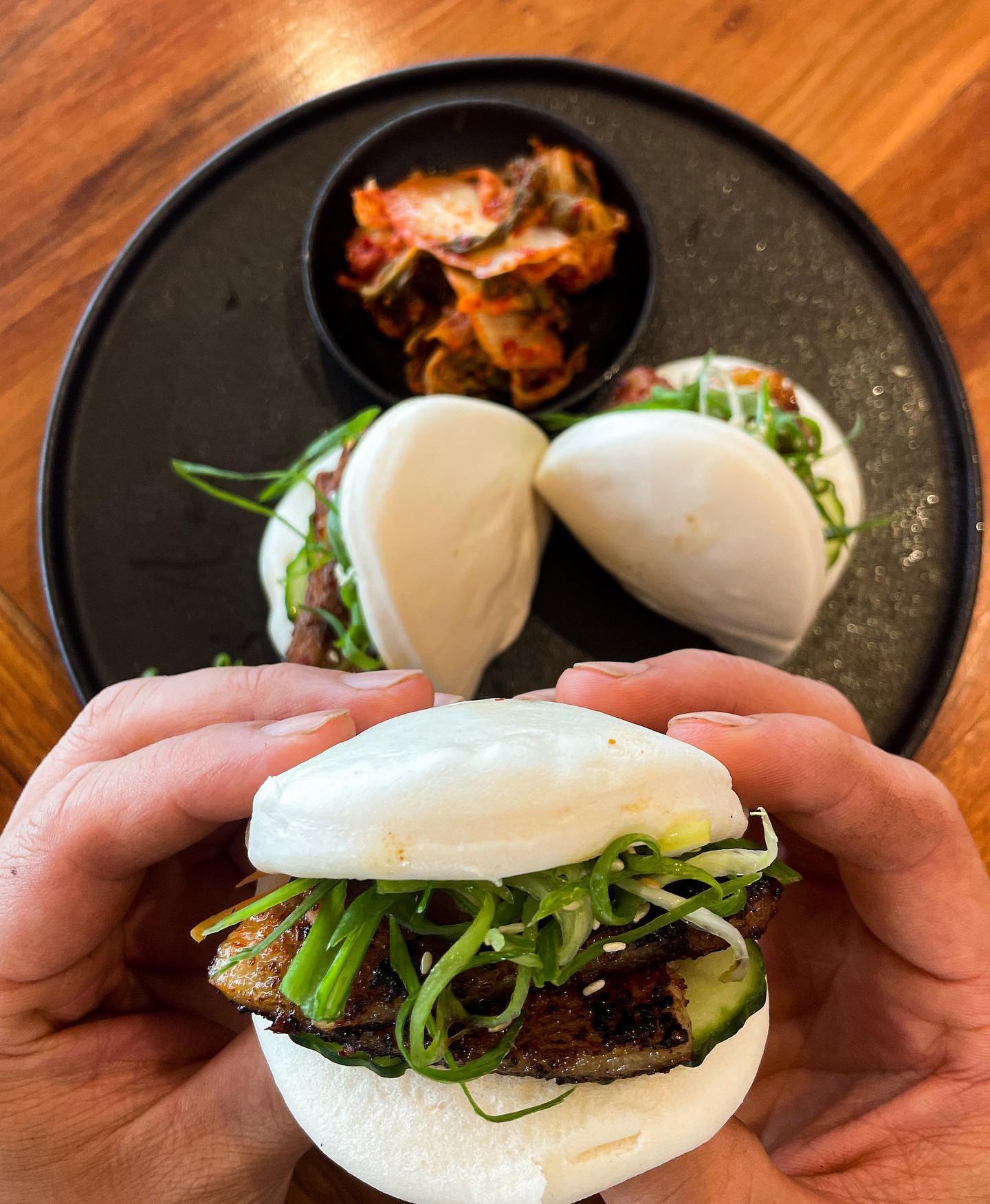 Hands holding bao buns filled with pork belly and greens