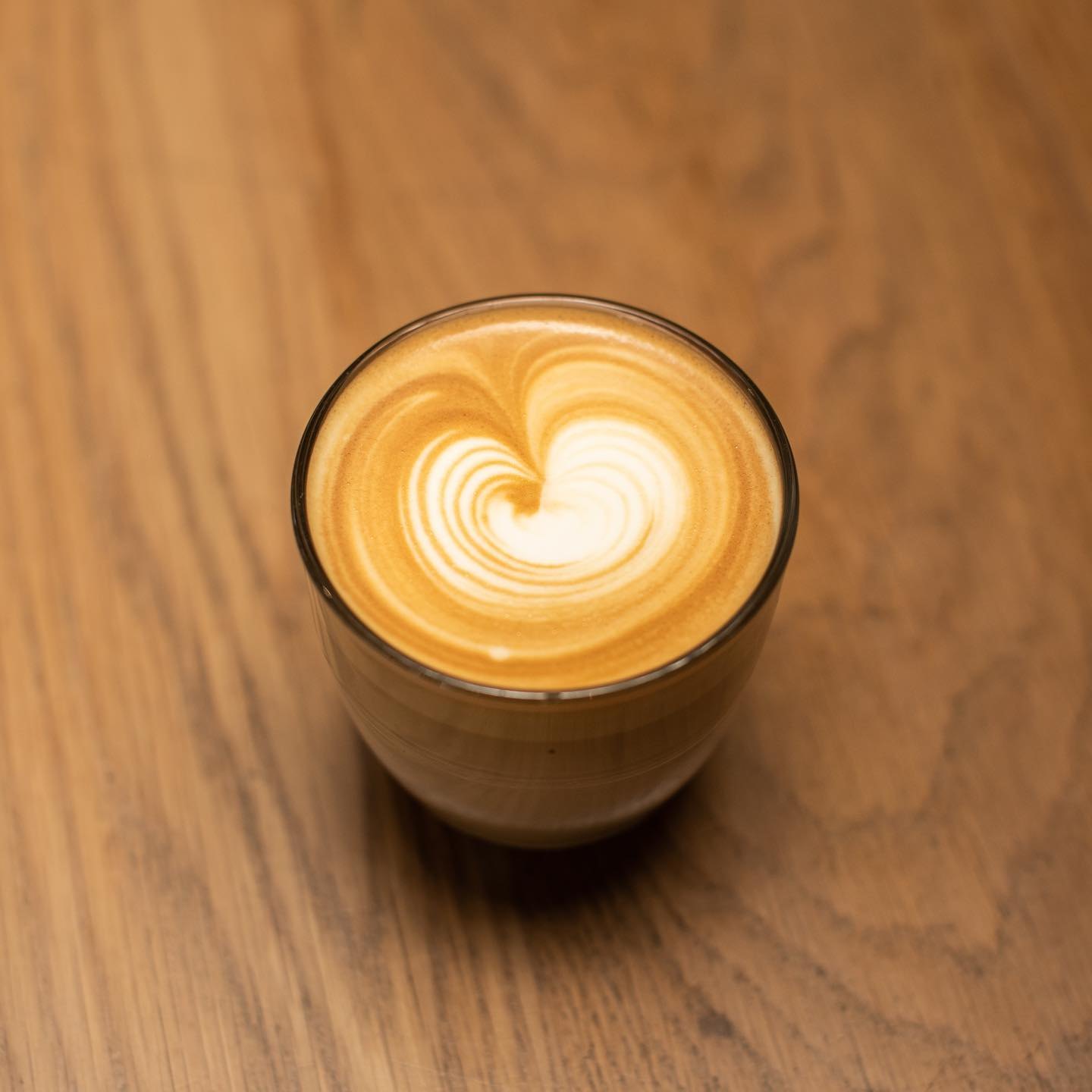 A latte with heart latte art in a glass on a timber table